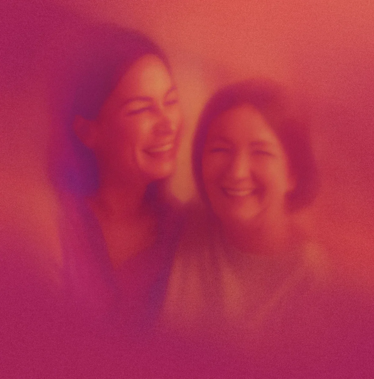 Two women smiling and laughing together with a warm pink and orange gradient overlay.